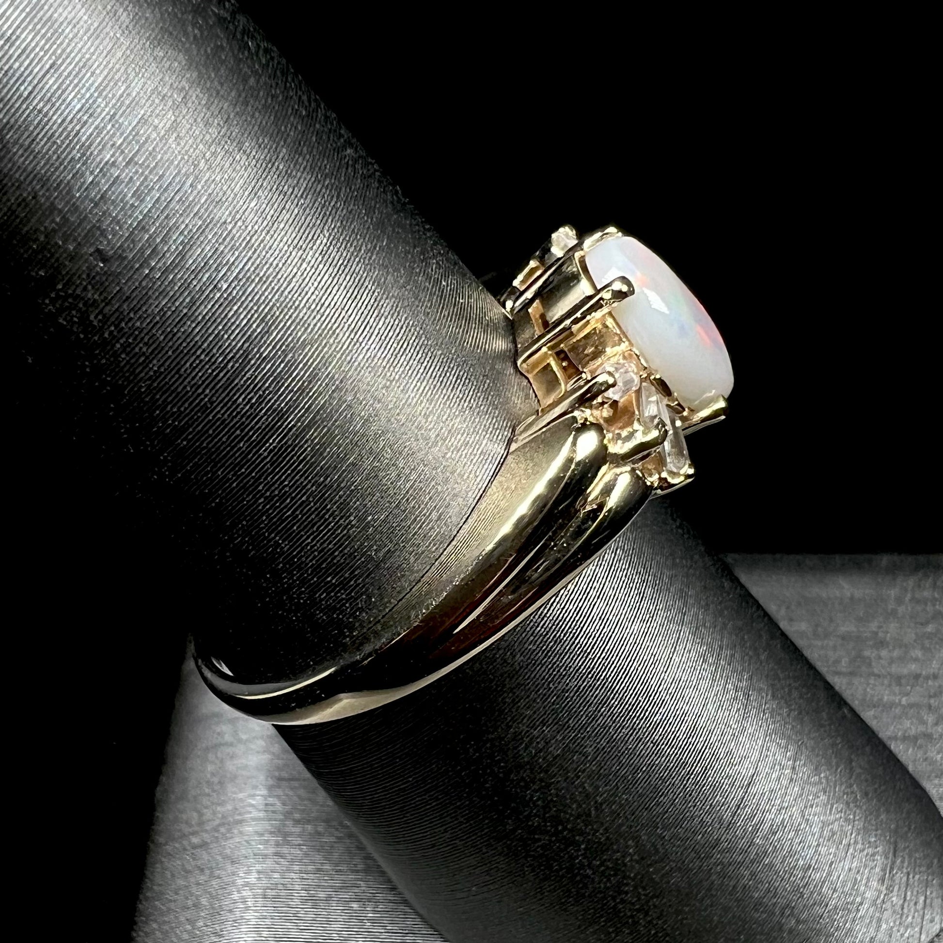 A yellow gold ring set with a natural Australian opal and tapered baguette cut cubic zirconia accents.