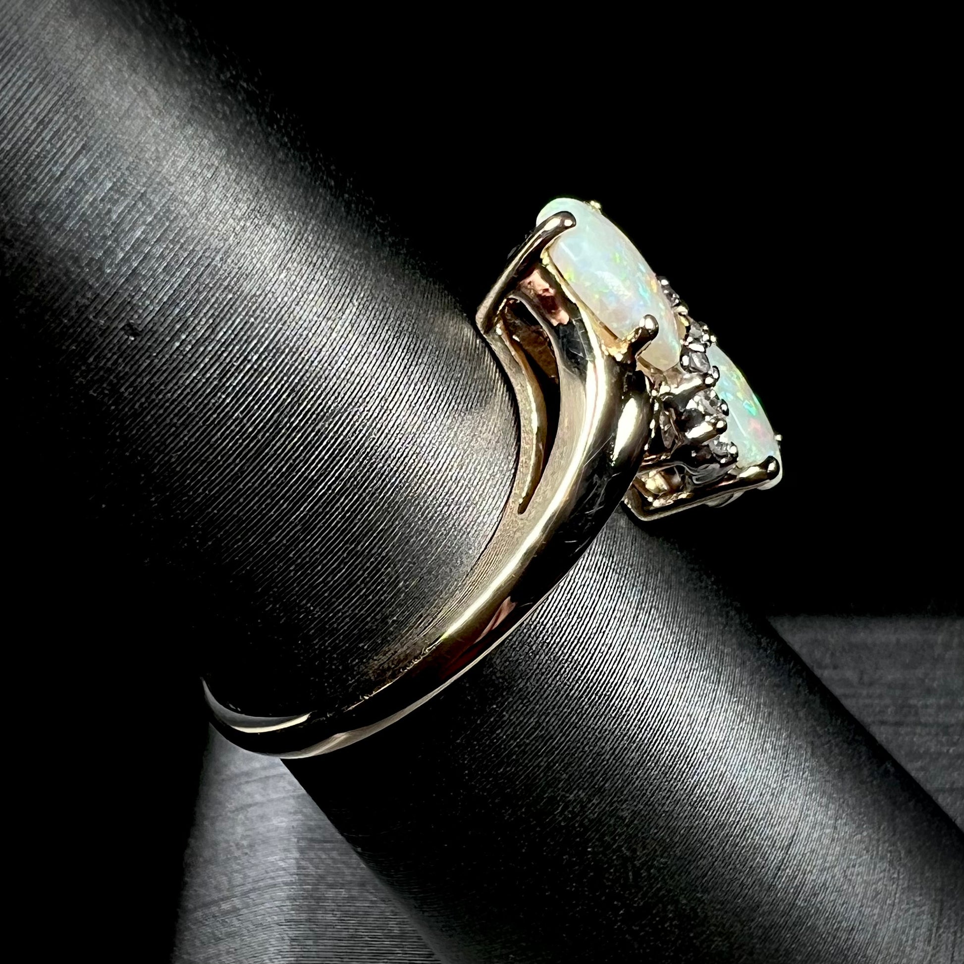 A yellow gold ring mounted with two pear shaped opals and diamond accents  The stones form an infinity shaped design.