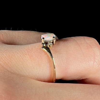 A dainty yellow gold opal and diamond-accented ring.  The opal has red and purple colors.