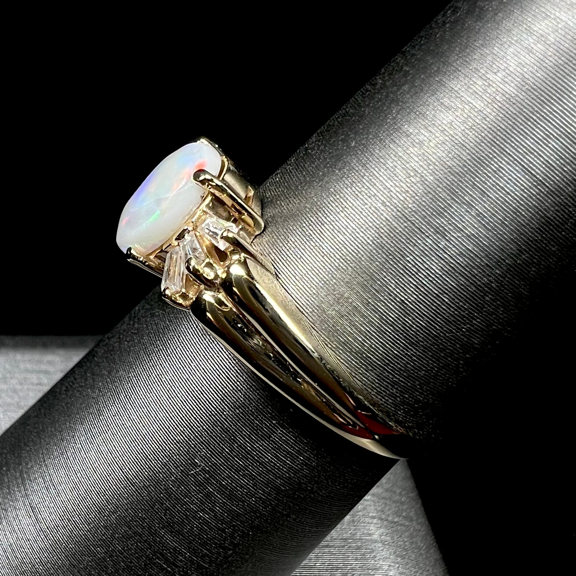 A yellow gold ring set with a natural Australian opal and tapered baguette cut cubic zirconia accents.