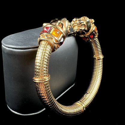 A 14 karat yellow gold hinged bangle bracelet featuring the motif of two panther heads.  There are yellow and red accent stones.