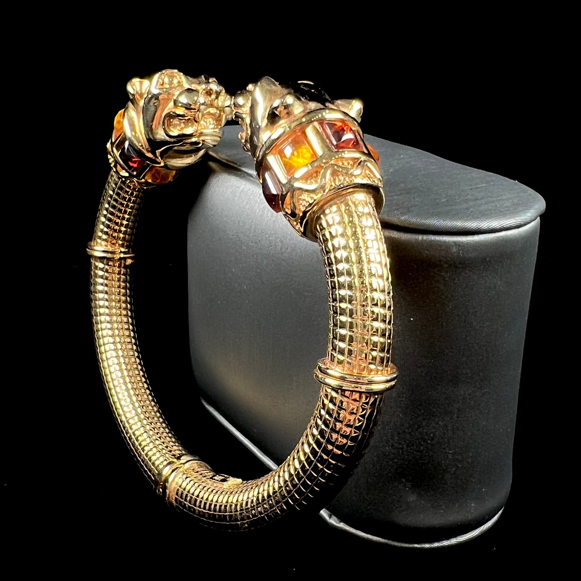 A 14 karat yellow gold hinged bangle bracelet featuring the motif of two panther heads.  There are yellow and red accent stones.