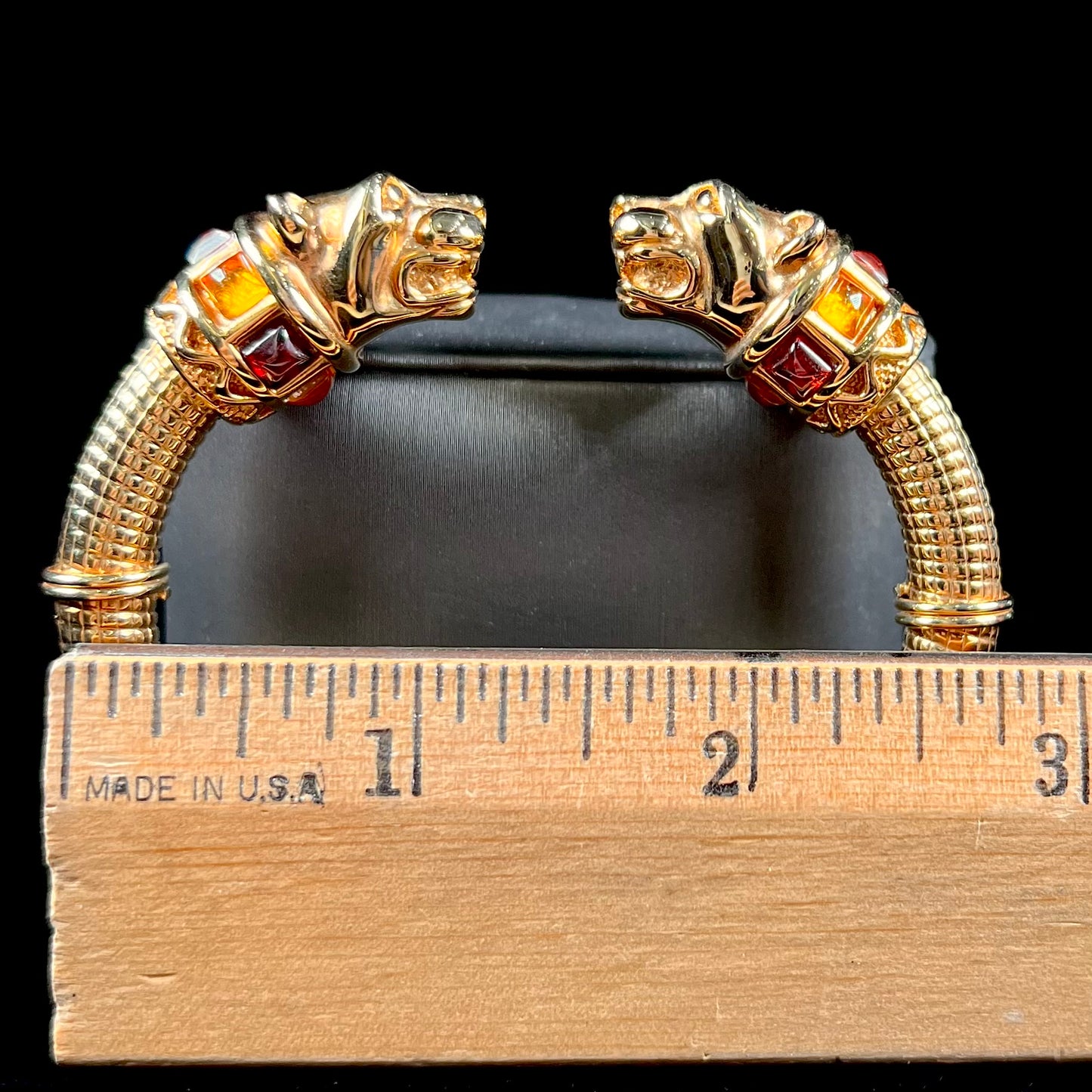 A 14 karat yellow gold hinged bangle bracelet featuring the motif of two panther heads.  There are yellow and red accent stones.