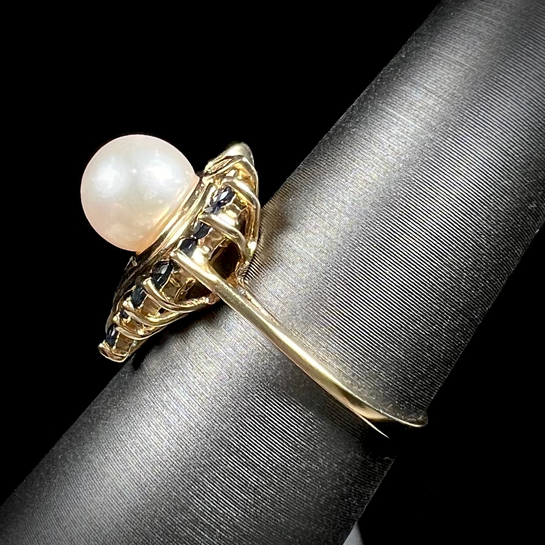 A yellow gold, heart shaped ring set with a freshwater pearl surrounded by blue sapphire and diamond accent stones.