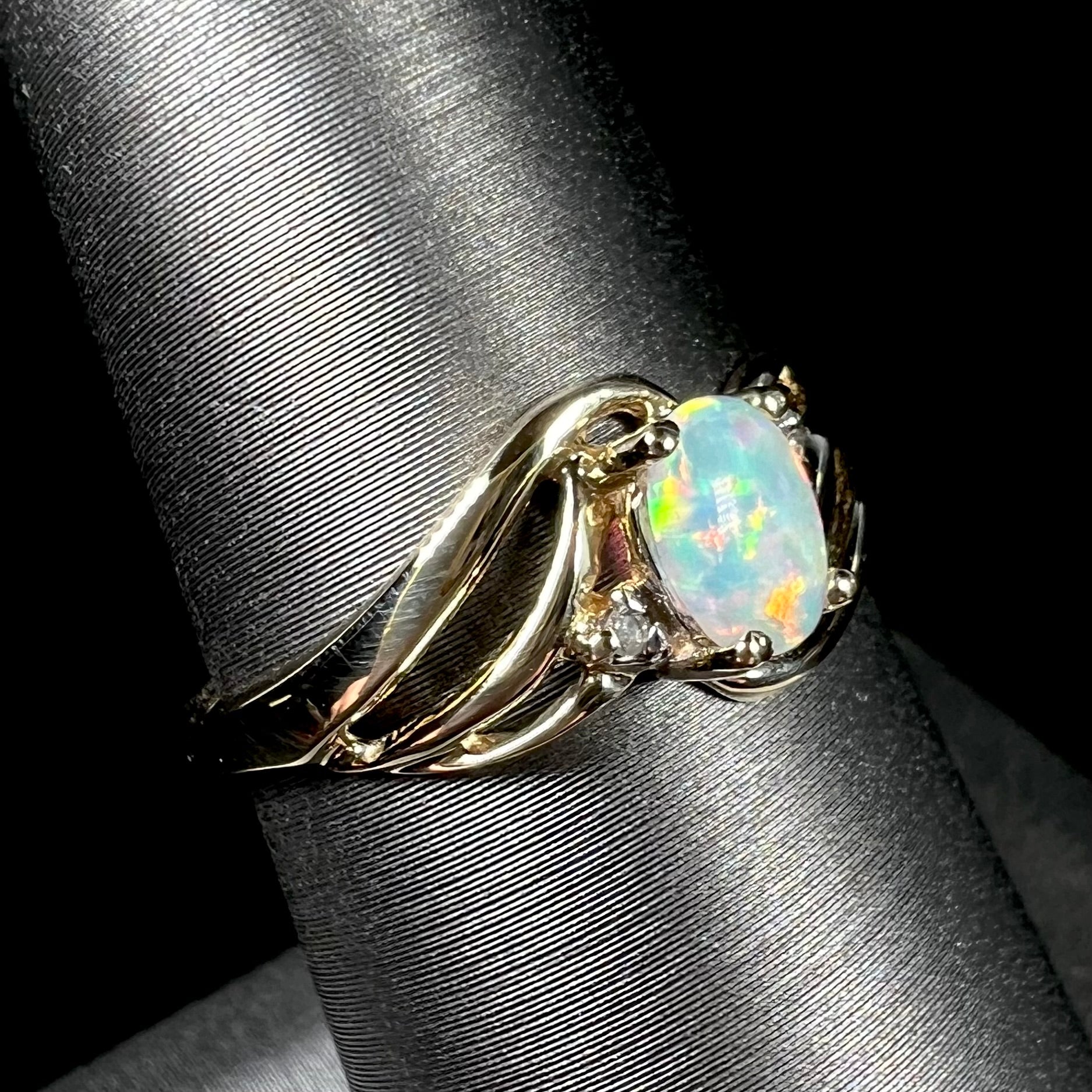 A yellow gold ring mounted with two diamond accents and an oval cut lab created opal.  The opal has bright red colors.