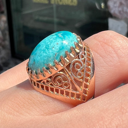 A yellow gold filigree style ring mounted with an oval Pilot Mountain turquoise stone.