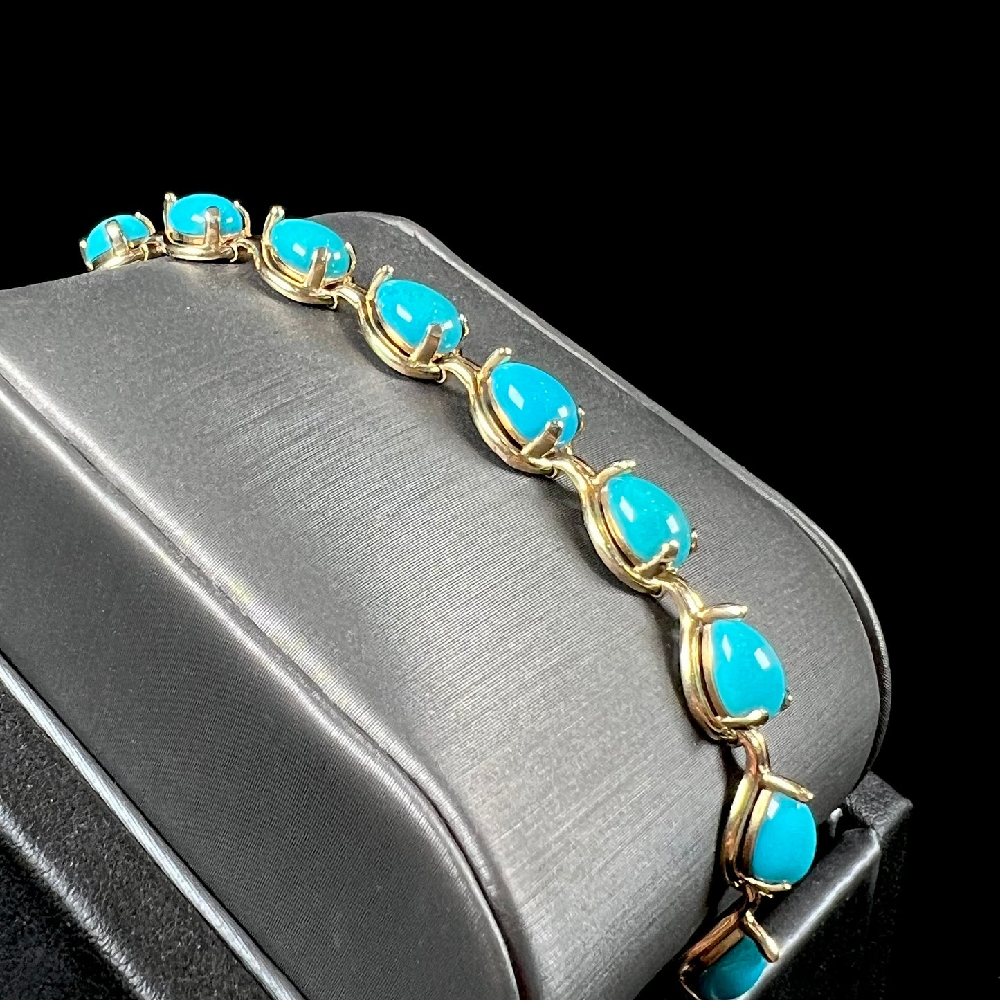 A ladies' yellow gold tennis style bracelet set with pear cabochon shaped natural Sleeping Beauty turquoise stones.