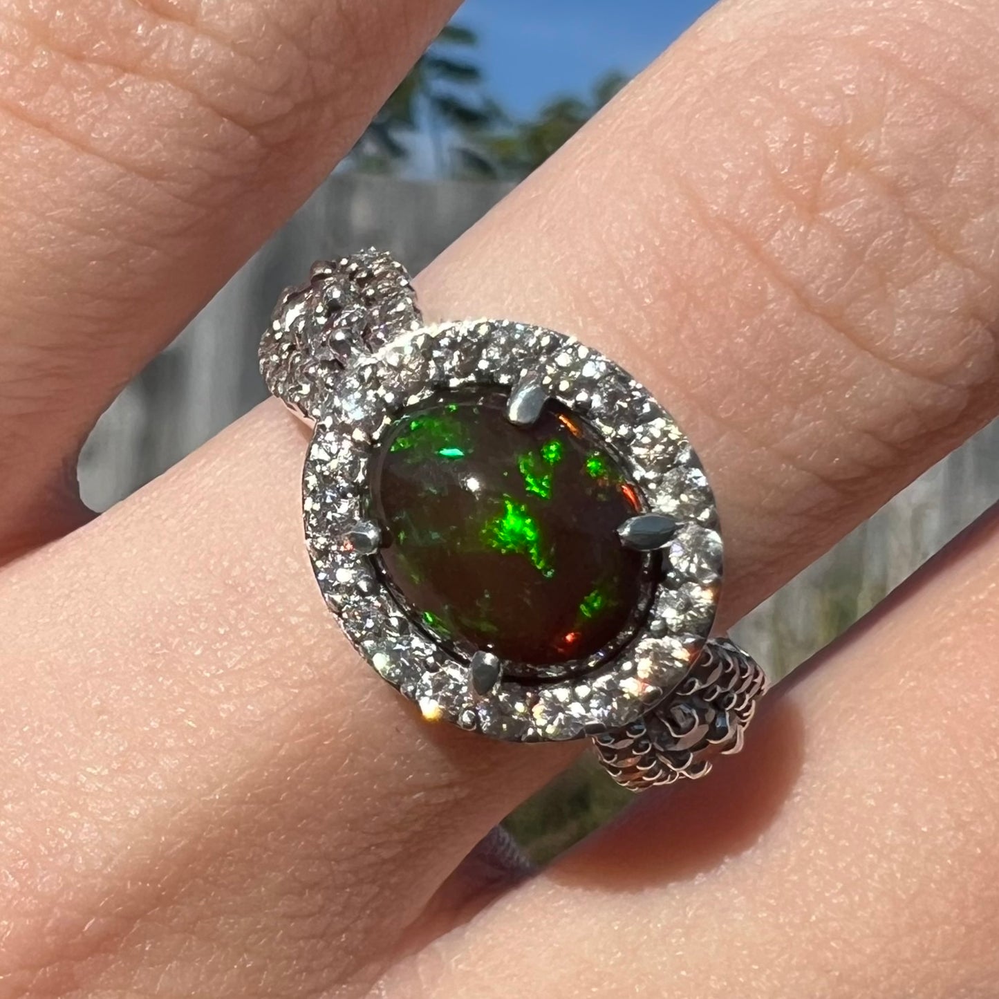 A CZ-accented sterling silver halo ring mounted with a smoked Ethiopian fire opal.  The opal plays green, red, and blue colors.