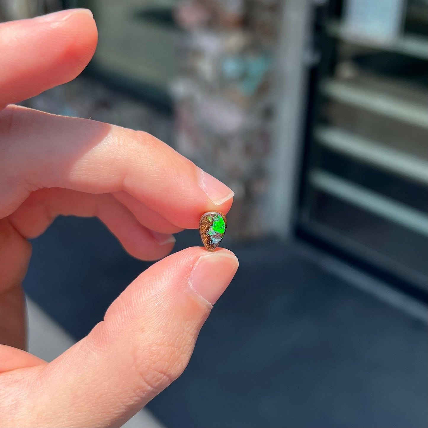 A loose, pear shaped boulder opal stone that flashes colors of green and blue.