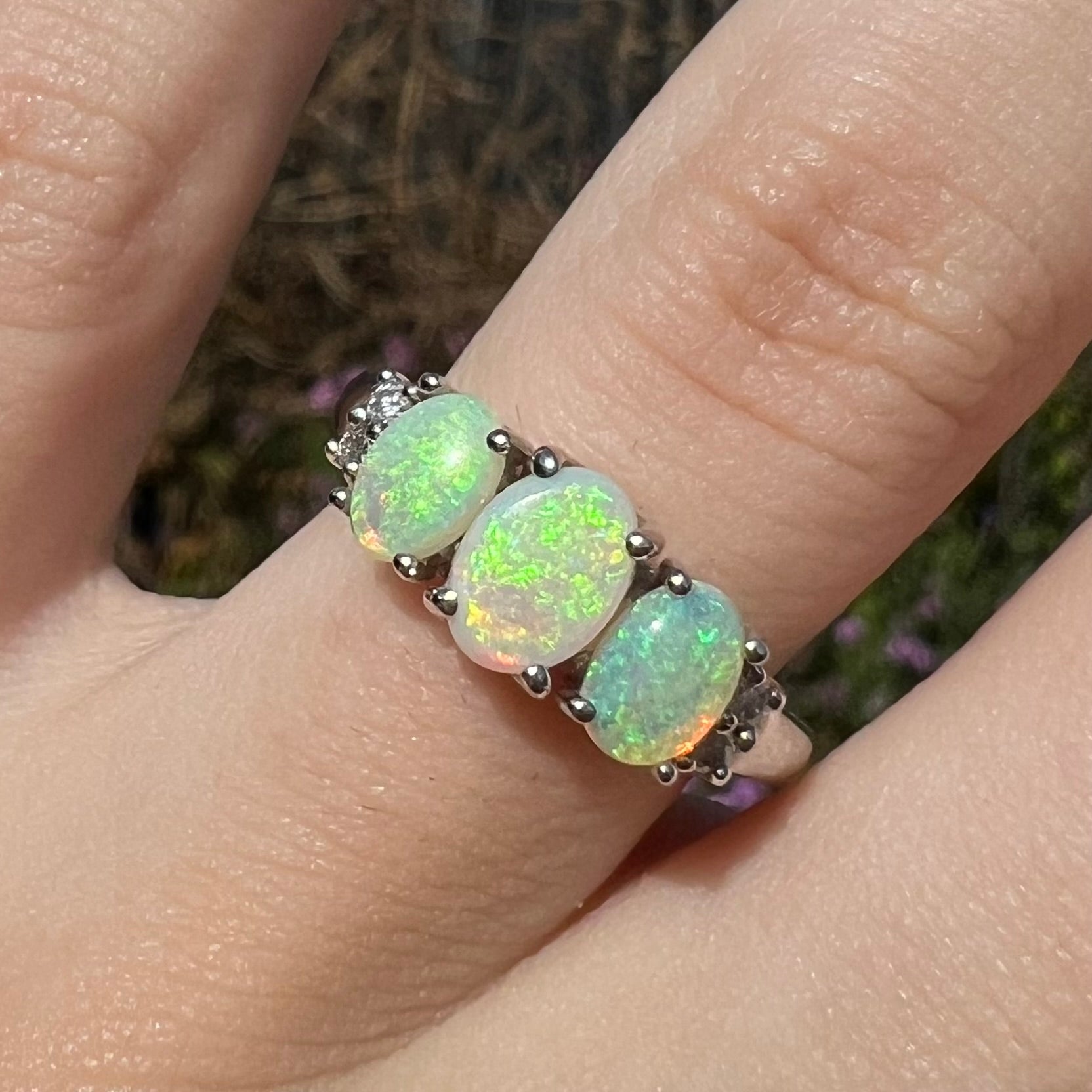 A ladies' white gold ring prong-set with three natural white opals and diamond accents.  The opals play a green color.