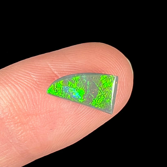 A loose, triangular shaped black opal stone from Lightning Ridge, Australia.  The opal has a bright green flash of color.