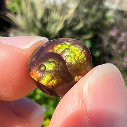 A loose, round Mexican fire agate stone.  The stone shines colors of green, yellow, and orange.