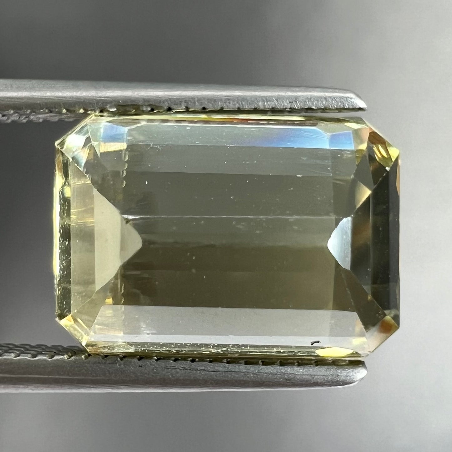 A loose, emerald cut hiddenite gemstone.  The stone is a light yellow green color.