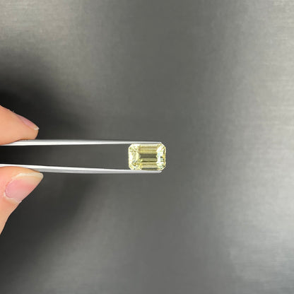 A loose, emerald cut hiddenite gemstone.  The stone is a light yellow green color.