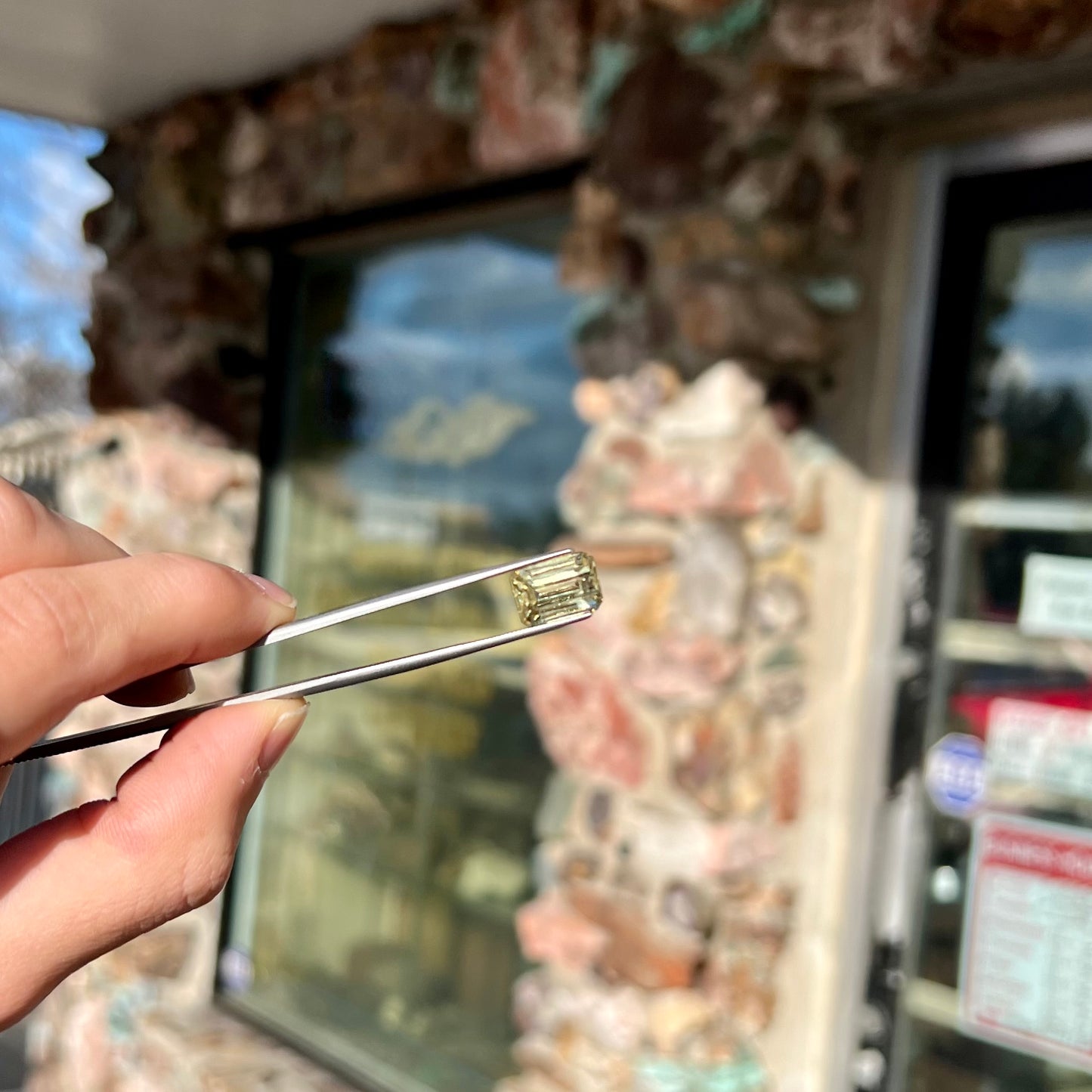 A loose, emerald cut hiddenite gemstone.  The stone is a light yellow green color.