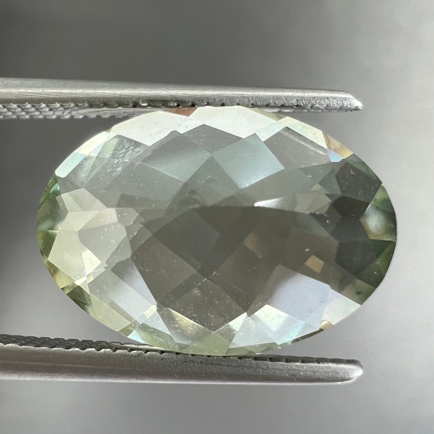 An oval checkerboard cut kiwi mystic topaz gemstone.  The stone is a light yellowish green color.