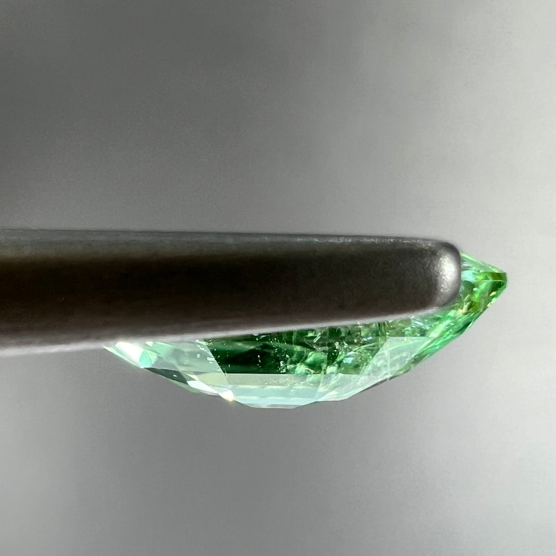 A faceted marquise cut electric green tourmaline gemstone.  The stone has an eye-visible rutile needle inclusion.