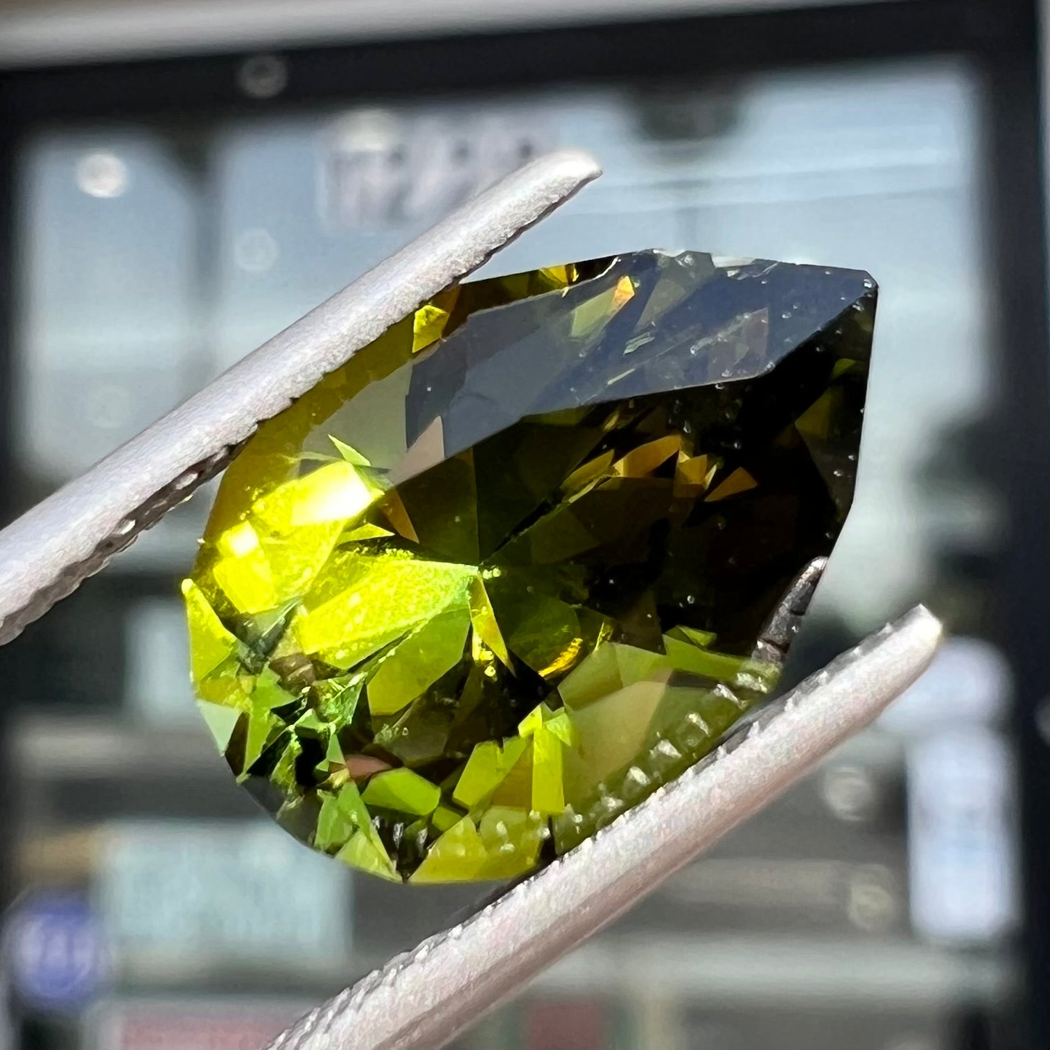 A loose, pear shaped green tourmaline gemstone.  The color is dark green with a yellow secondary hue.