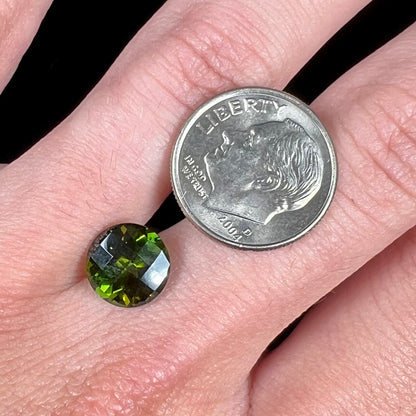 A loose, round checkerboard cut green tourmaline stone with flashes of yellow.