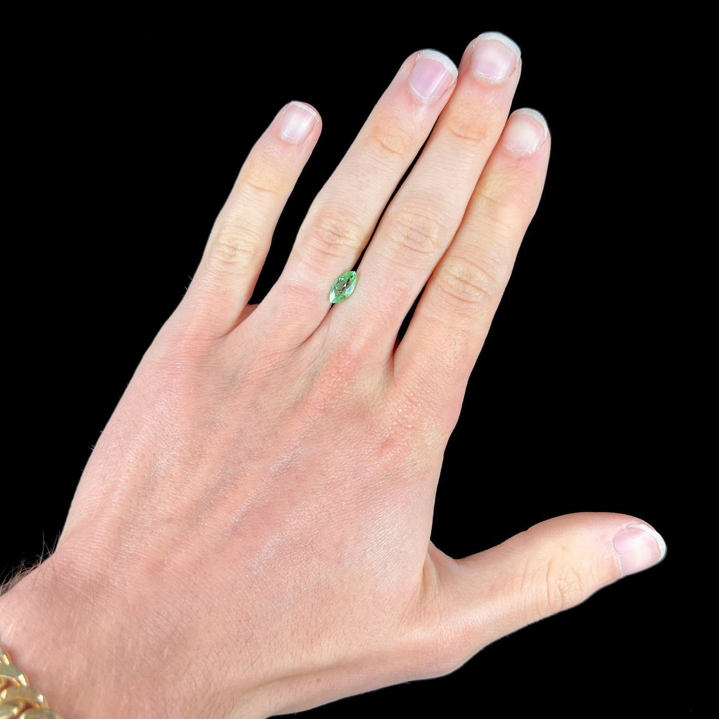 A faceted marquise cut electric green tourmaline gemstone.  The stone has an eye-visible rutile needle inclusion.