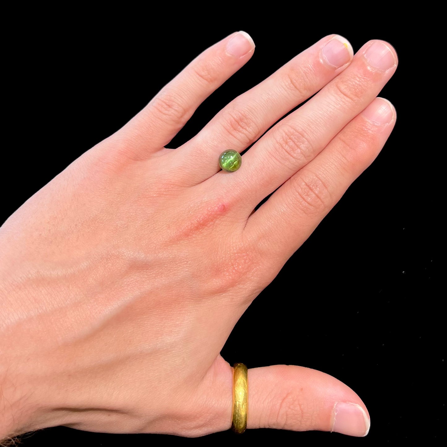 A loose, round cabochon cut green tourmaline stone that displays a cat's eye phenomenon.