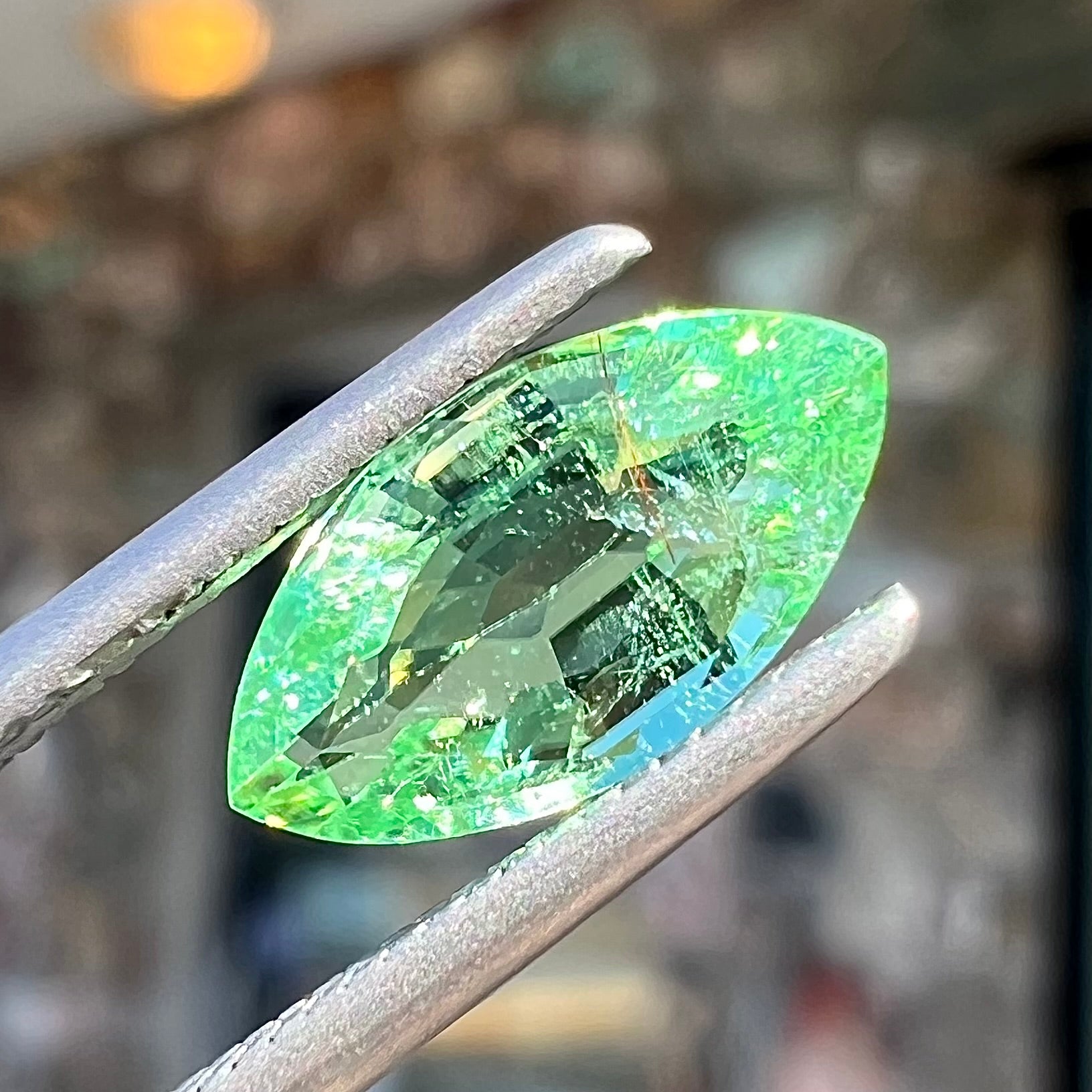 A faceted marquise cut electric green tourmaline gemstone.  The stone has an eye-visible rutile needle inclusion.