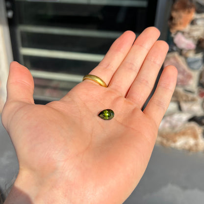 A loose, pear shaped green tourmaline gemstone.  The color is dark green with a yellow secondary hue.