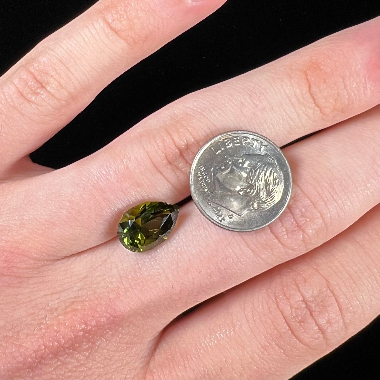 A loose, pear shaped green tourmaline gemstone.  The color is dark green with a yellow secondary hue.