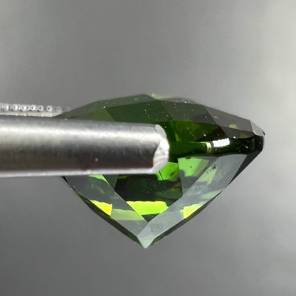 A loose, round checkerboard cut green tourmaline stone with flashes of yellow.