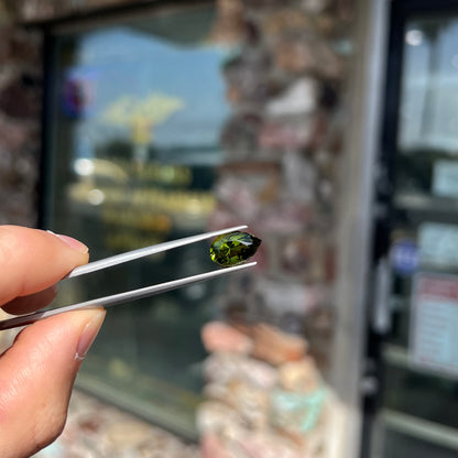 A loose, pear shaped green tourmaline gemstone.  The color is dark green with a yellow secondary hue.