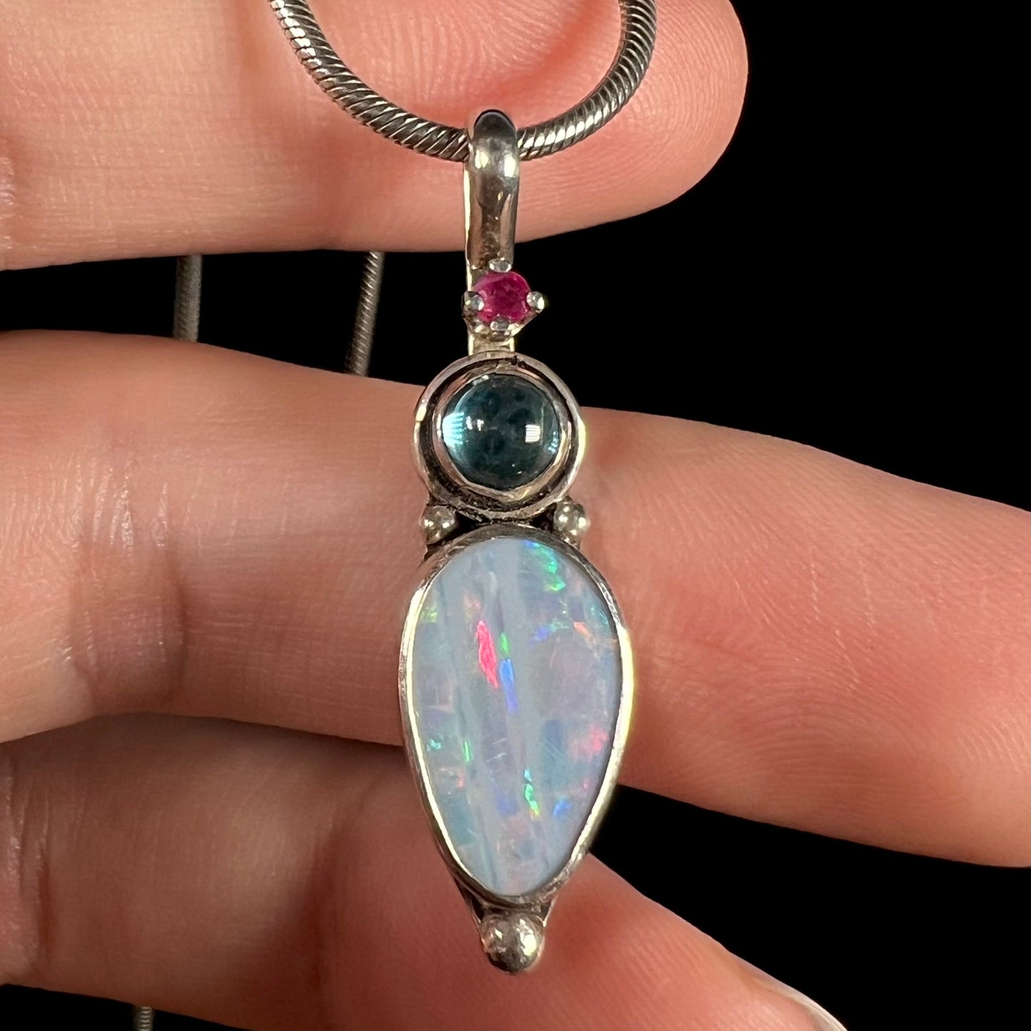 A sterling silver necklace shaped like a child, mounted with an opal doublet, a ruby, and a blue piece of glass.