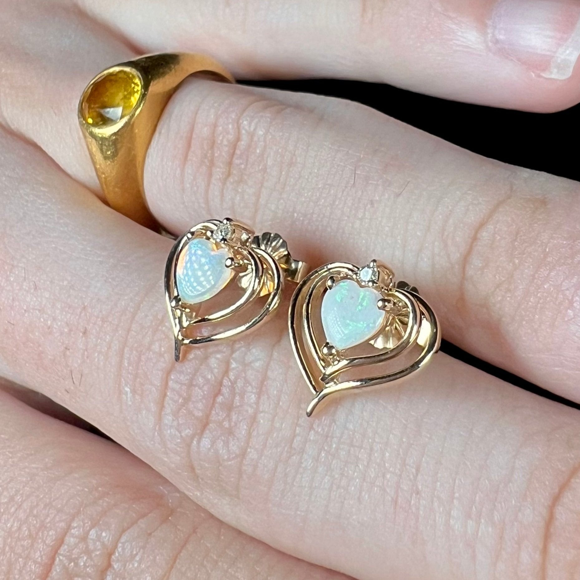 A pair of heart shaped, yellow gold opal stud earrings.  The top of the earrings have a diamond accent.