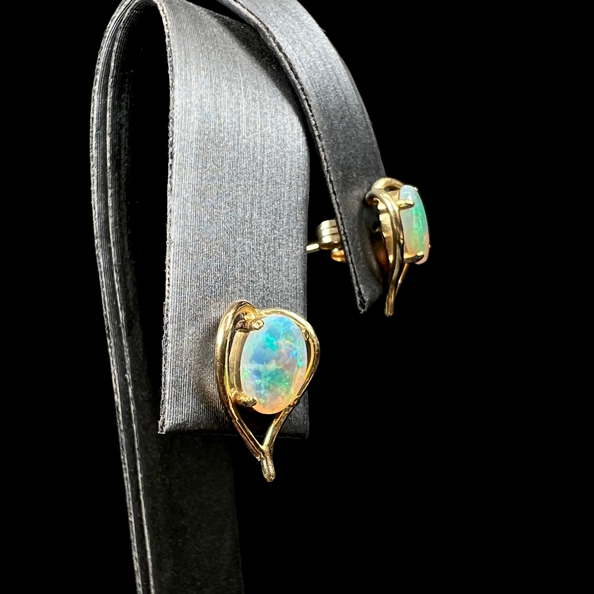 A pair of yellow gold, heart shaped stud earrings set with oval cabochon cut natural opal stones.