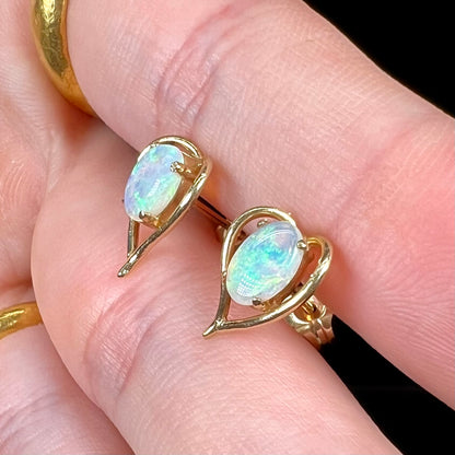 A pair of yellow gold, heart shaped stud earrings set with oval cabochon cut natural opal stones.