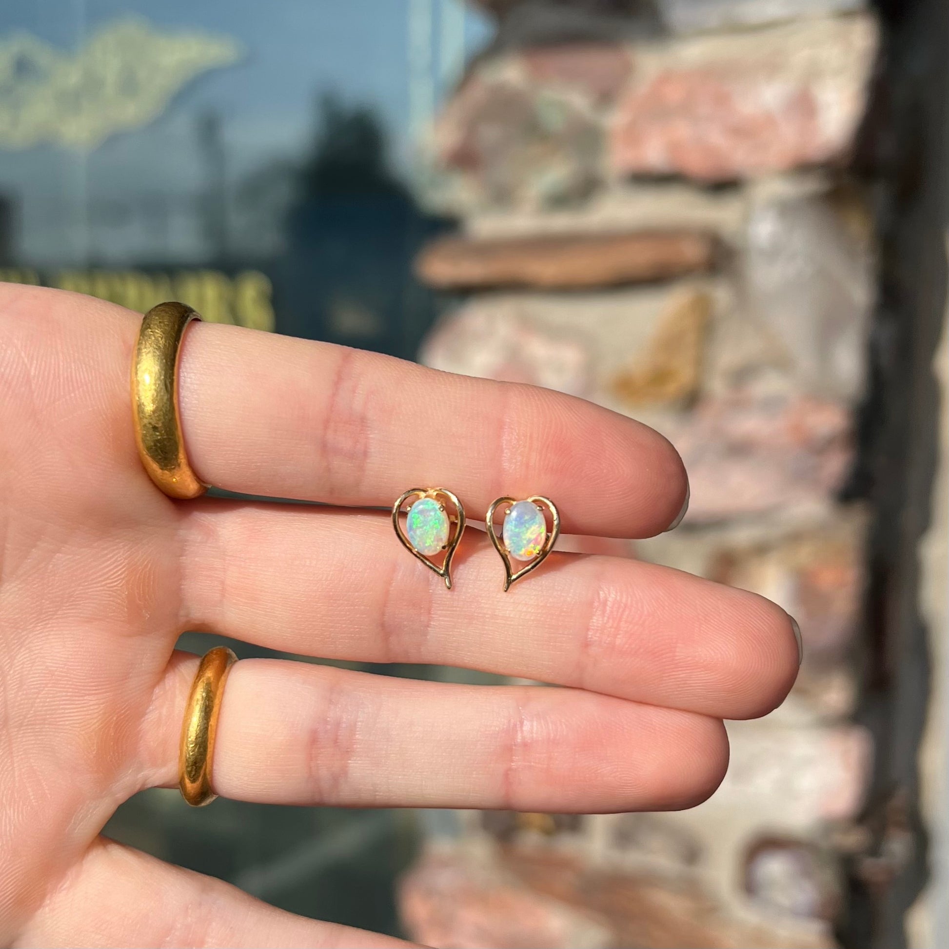 A pair of yellow gold, heart shaped stud earrings set with oval cabochon cut natural opal stones.