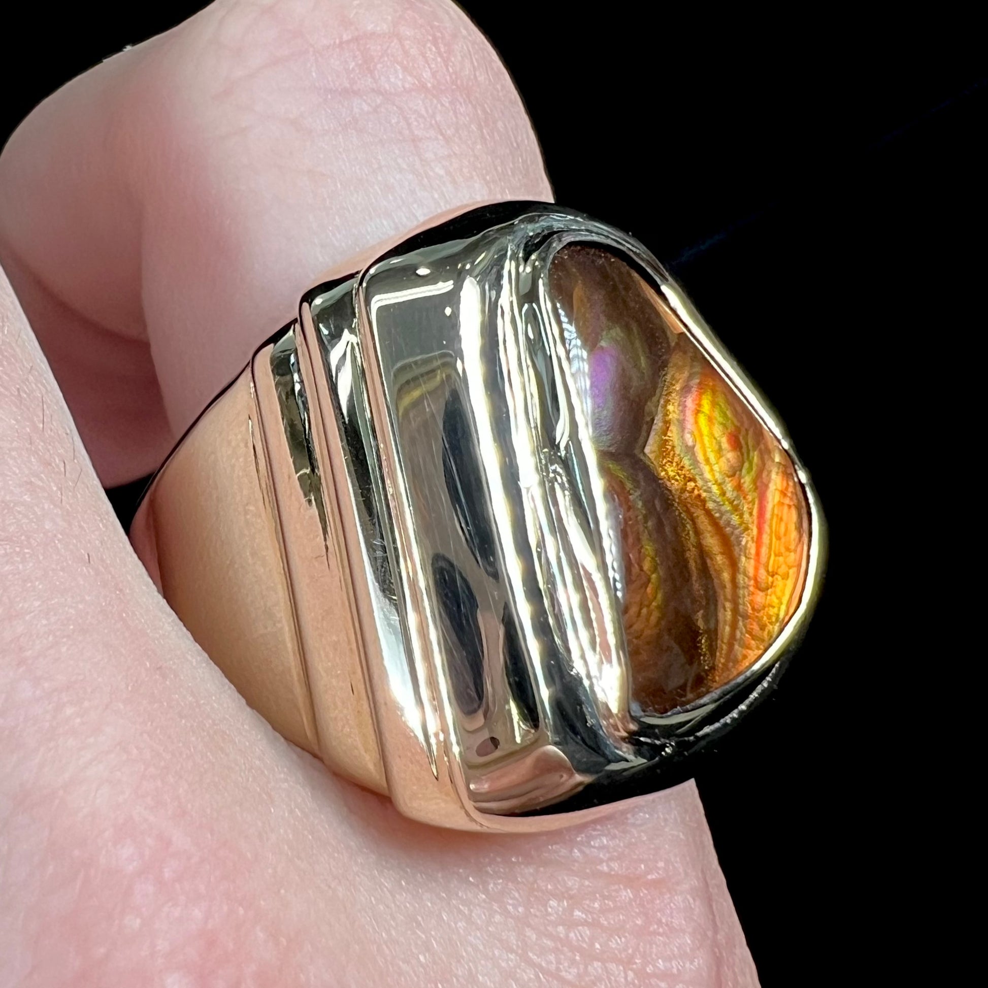 A heavy, yellow gold men's ring mounted with a Mexican fire agate stone.  The fire agate has orange, green, red, and purple colors.