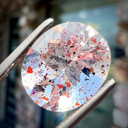 A loose, faceted oval cut lepidocrocite quartz stone.  The stone has red and black inclusions.