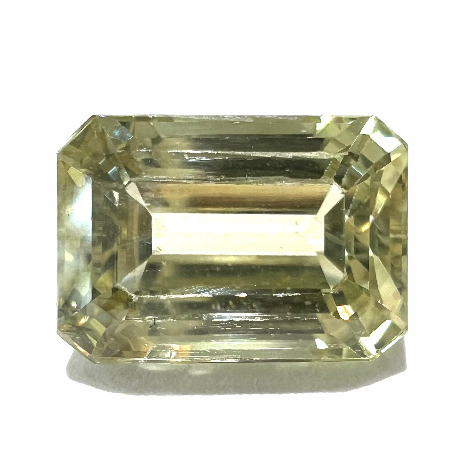 A loose, emerald cut hiddenite gemstone.  The stone is a light yellow green color.