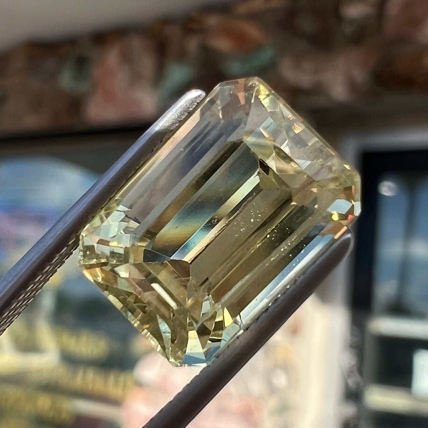 A loose, emerald cut hiddenite gemstone.  The stone is a light yellow green color.