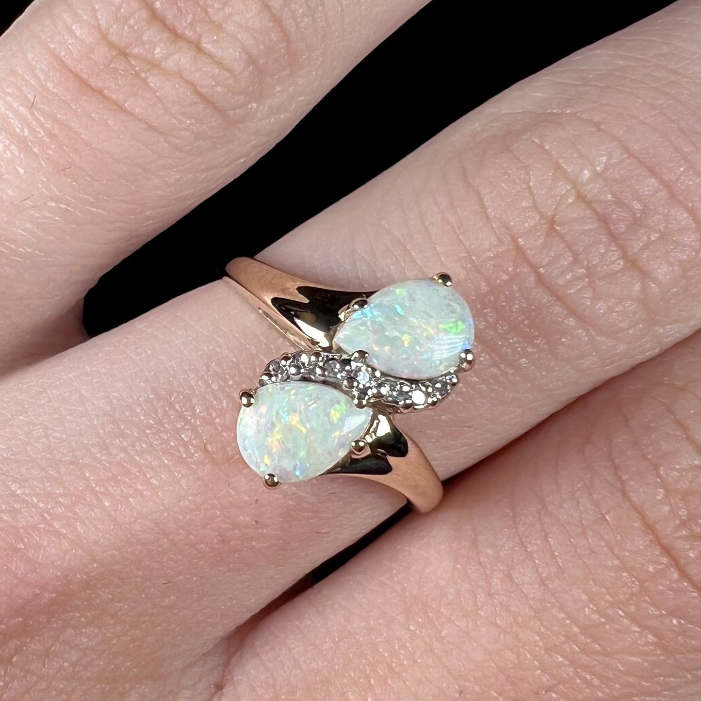 A yellow gold ring mounted with two pear shaped opals and diamond accents  The stones form an infinity shaped design.