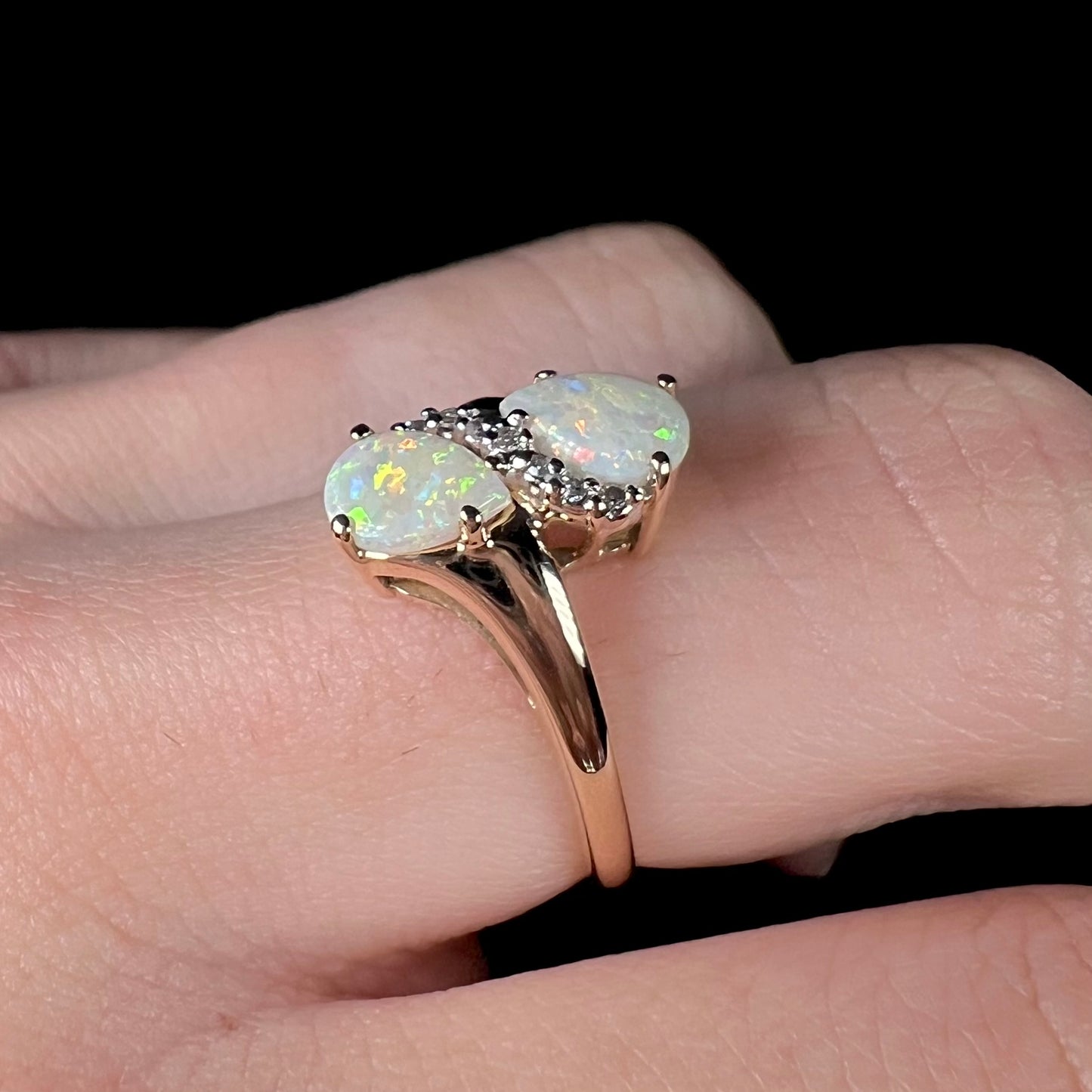 A yellow gold ring mounted with two pear shaped opals and diamond accents  The stones form an infinity shaped design.