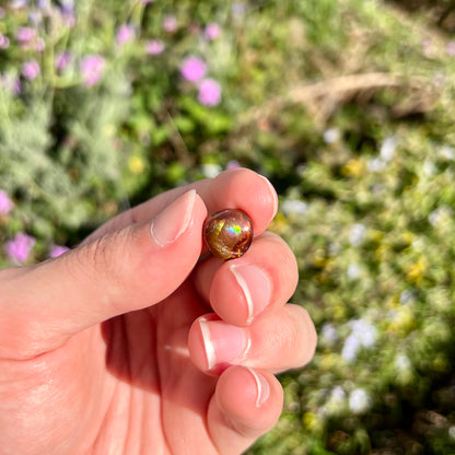 A loose, round cabochon cut Mexican fire agate gemstone.  The stone has a sagenite inclusion.