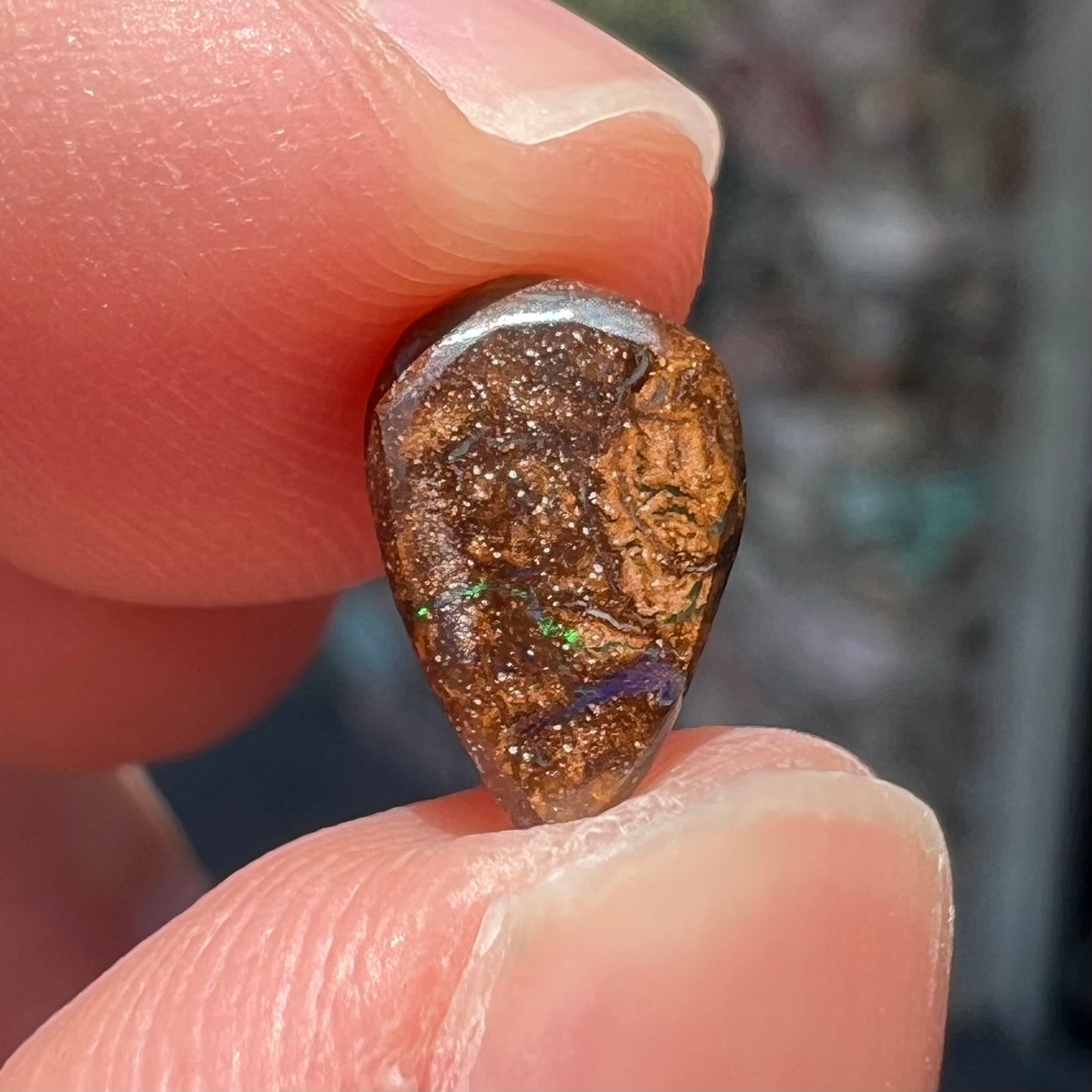 A loose, pear shaped boulder opal stone that flashes colors of green and blue.