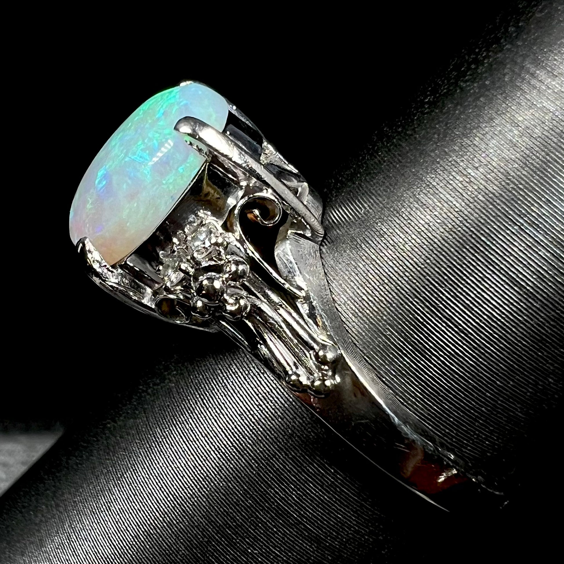 A platinum filigree ring mounted with a blue-green crystal opal and diamond accents.