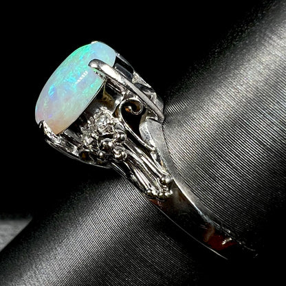 A platinum filigree ring mounted with a blue-green crystal opal and diamond accents.