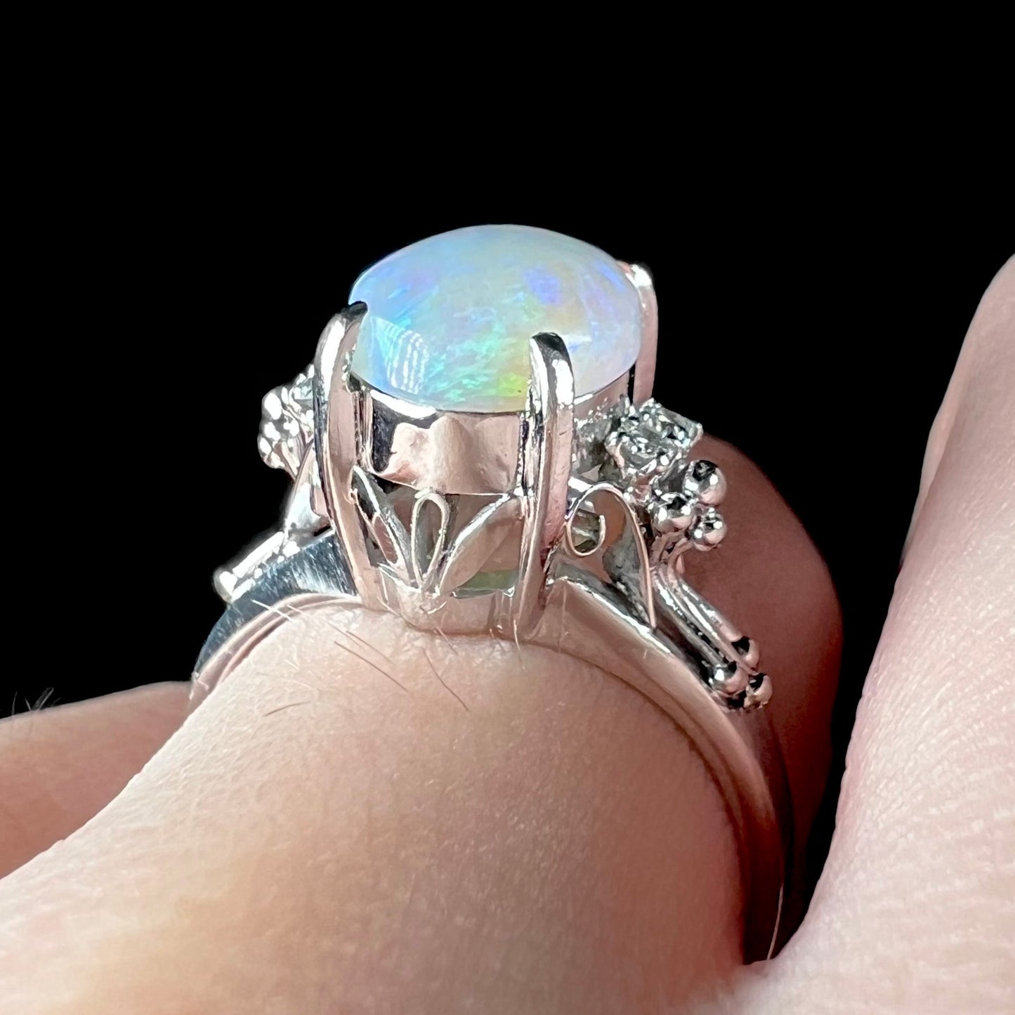 A platinum filigree ring mounted with a blue-green crystal opal and diamond accents.