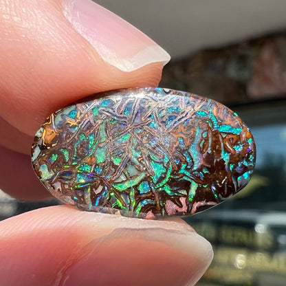 A loose, oval cabochon cut Koroit boulder opal stone.  The opal has green and blue veins.