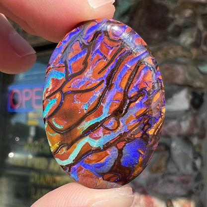 A loose, oval cabochon cut boulder opal from Koroit, Australia.  The opal has violet and purple veins.