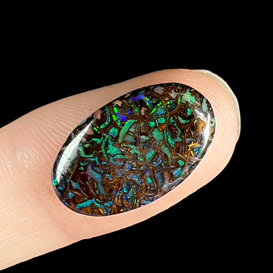 A loose, oval cabochon cut Koroit boulder opal stone.  The opal has green and blue veins.