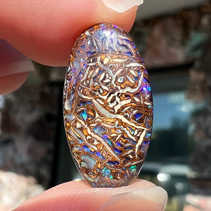 An oval cabochon cut Koroit boulder matrix opal stone.  The opal has blue colors.